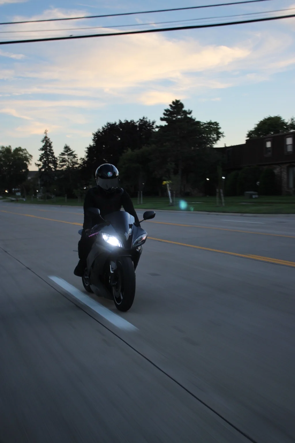 Motorcyclist riding toward the camera beneath a soft dusk sky