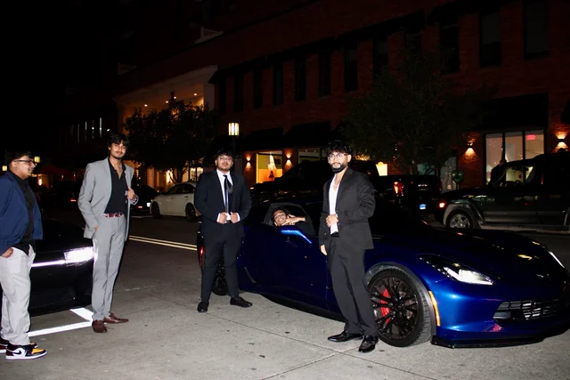 Editorial group portrait gathered around a blue Corvette at night