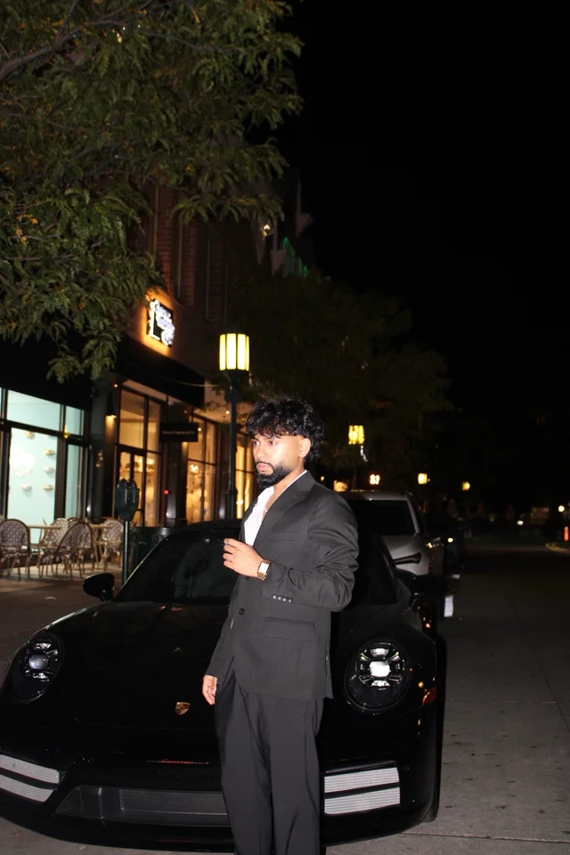 Nighttime portrait beside a black Porsche under warm streetlights